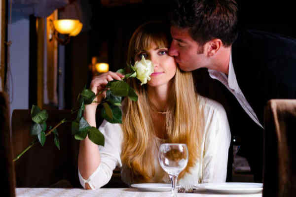 Hombre da un beso a mujer con una rosa en una cena
